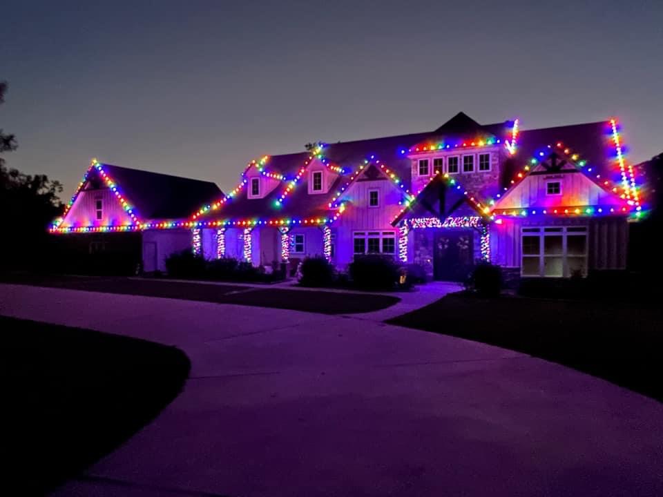 Colorful roofline lights on a large house at dusk